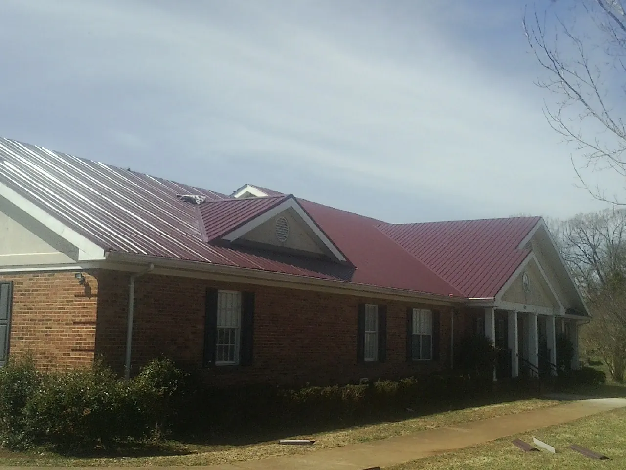 Red metal roof with gabled entries on a long brick building, from a Hail Damage Roof Repair job in Bolivia