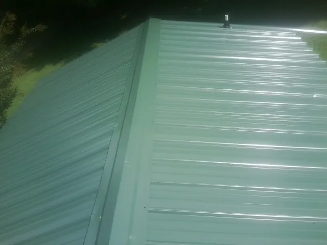 New green metal panels meeting at the ridge of a roof — Flat Roof Repair work by our crew in Bolivia