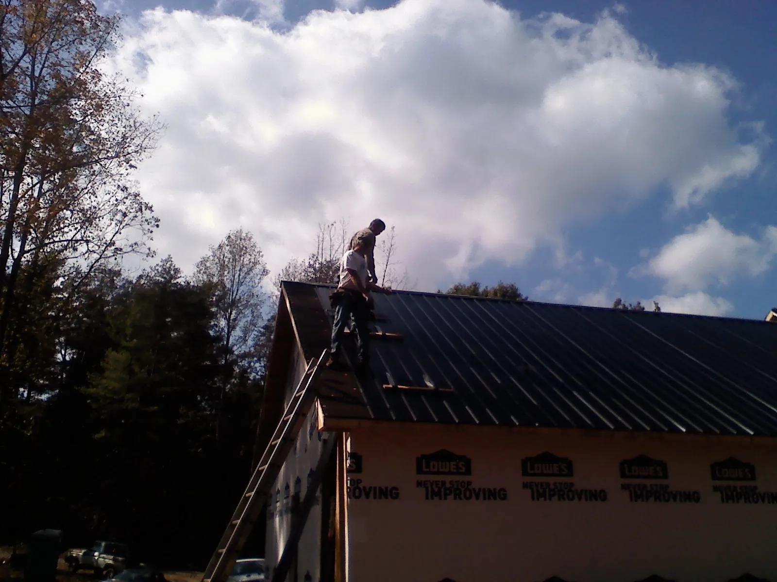 Roofer fastening dark metal panels high against a cloudy sky, from a Roof Inspection job in Bolivia