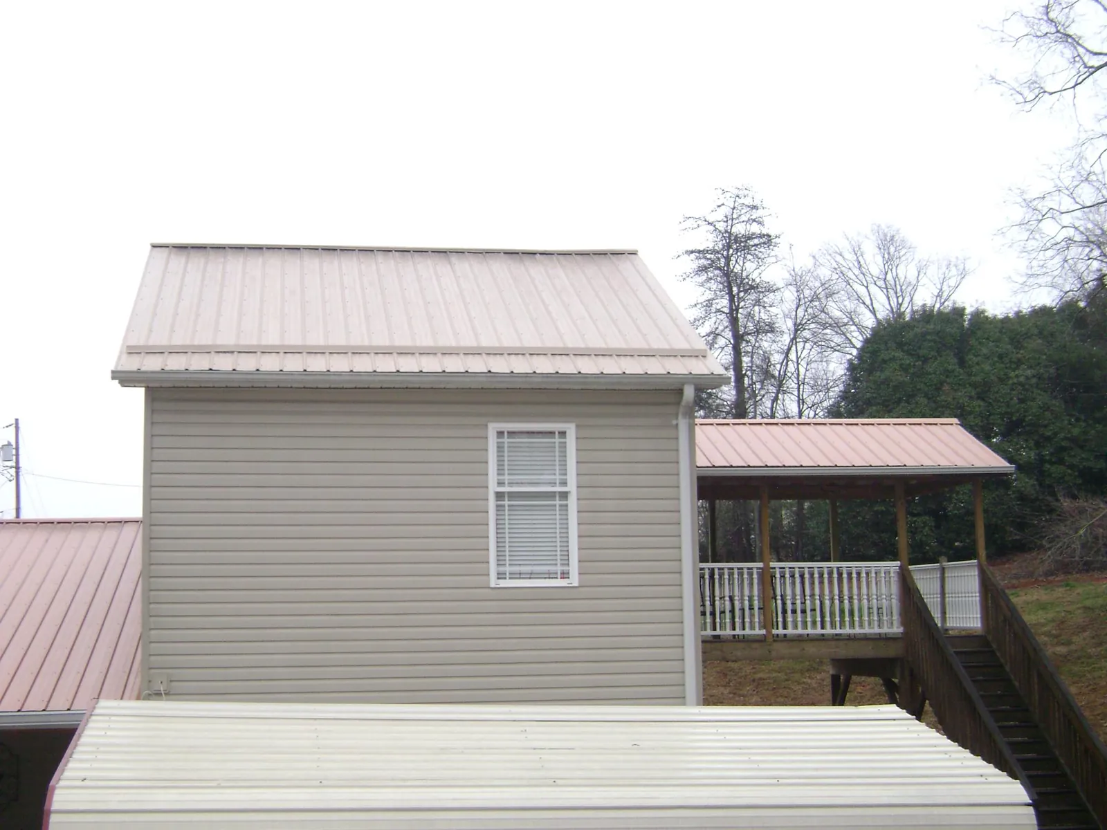 Tan metal roofs on a two story addition and attached porch, from a Roof Replacement job in Bolivia